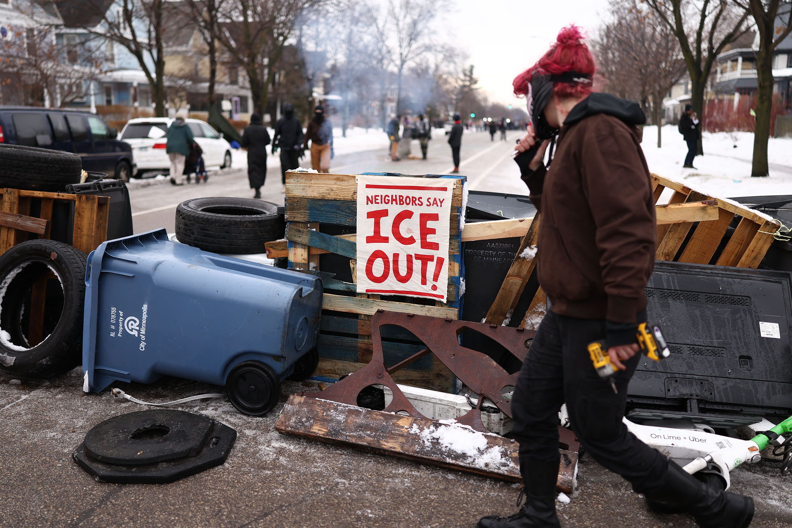 Figure walks by a makeshift wall and a sign that reads “Neighbors say ICE out”